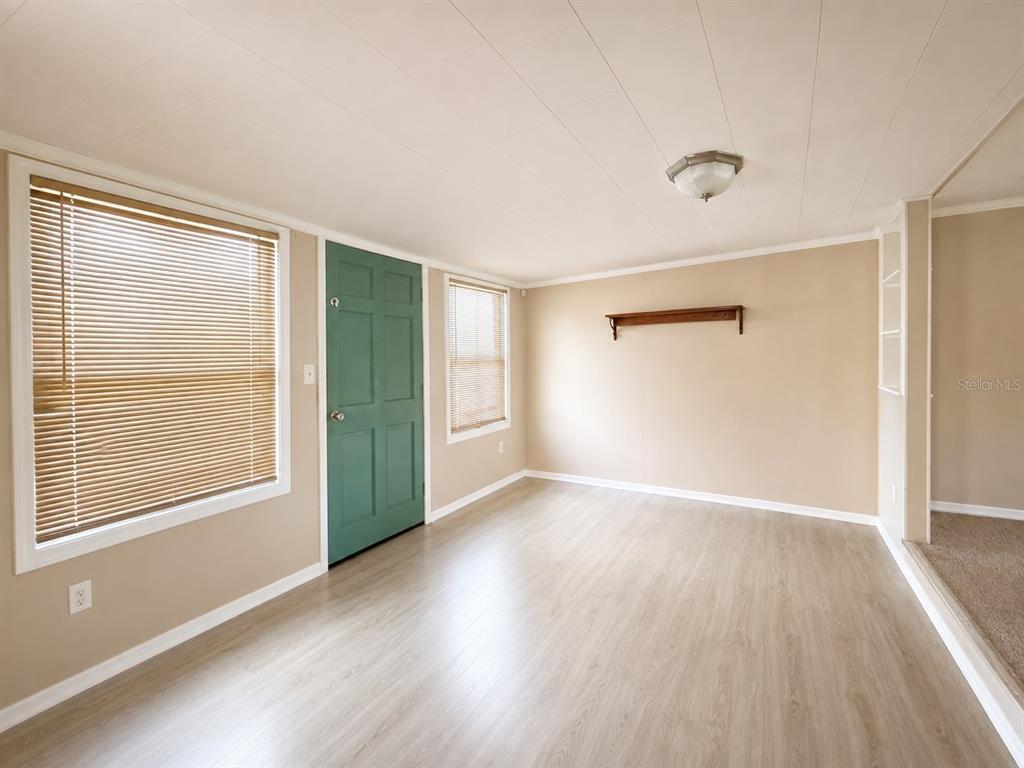 A room with light wood-look flooring, beige walls, a green door, and a ceiling light — 141 ROBINHOOD DRIVE, DELAND, FL