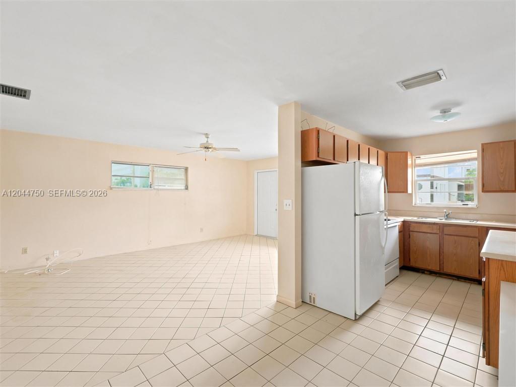 An open-concept kitchen and living area features light-colored tile flooring and wooden cabinetry — 211 SE 10th St, Hallandale Beach FL 33009, HALLANDALE BEACH, FL