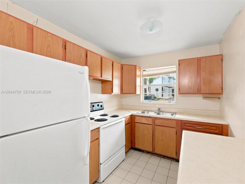 A kitchen features wood cabinets, white appliances, a double sink, and tiled flooring — 211 SE 10th St, Hallandale Beach FL 33009, HALLANDALE BEACH, FL