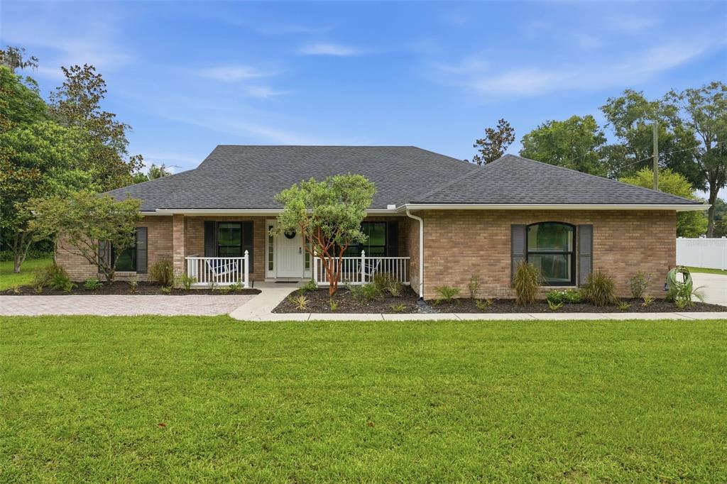 A single-story brick house with a dark shingled roof and a white front porch railing — 535 E PLYMOUTH AVENUE, DELAND, FL