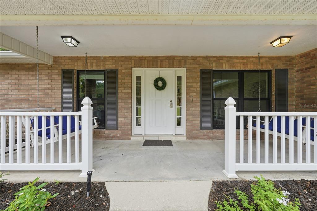 A brick house exterior features a covered front porch with white railings and two swings — 535 E PLYMOUTH AVENUE, DELAND, FL
