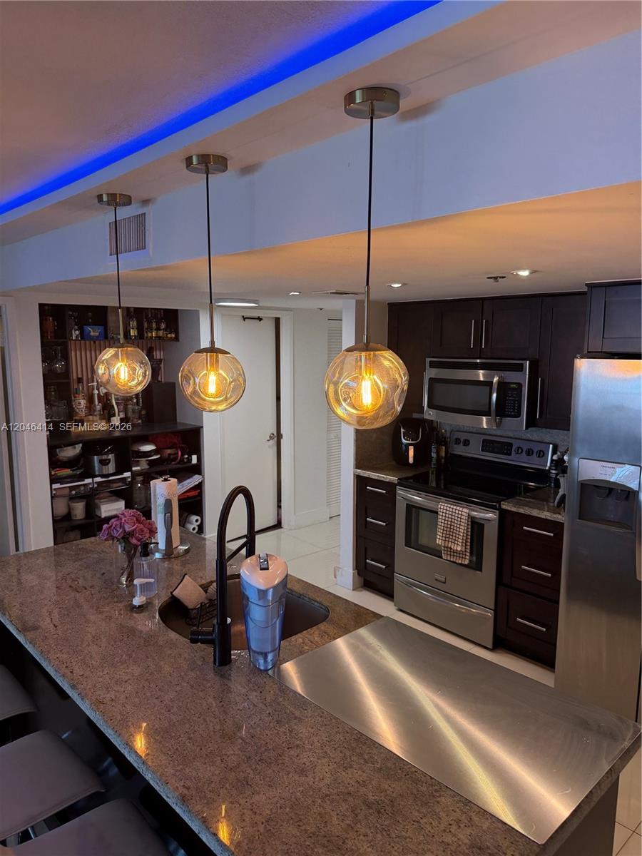 A kitchen features dark wood cabinets, stainless steel appliances, a granite island, and pendant lighting — 1717 N Bayshore Dr # 2847, Miami FL 33132, MIAMI, FL
