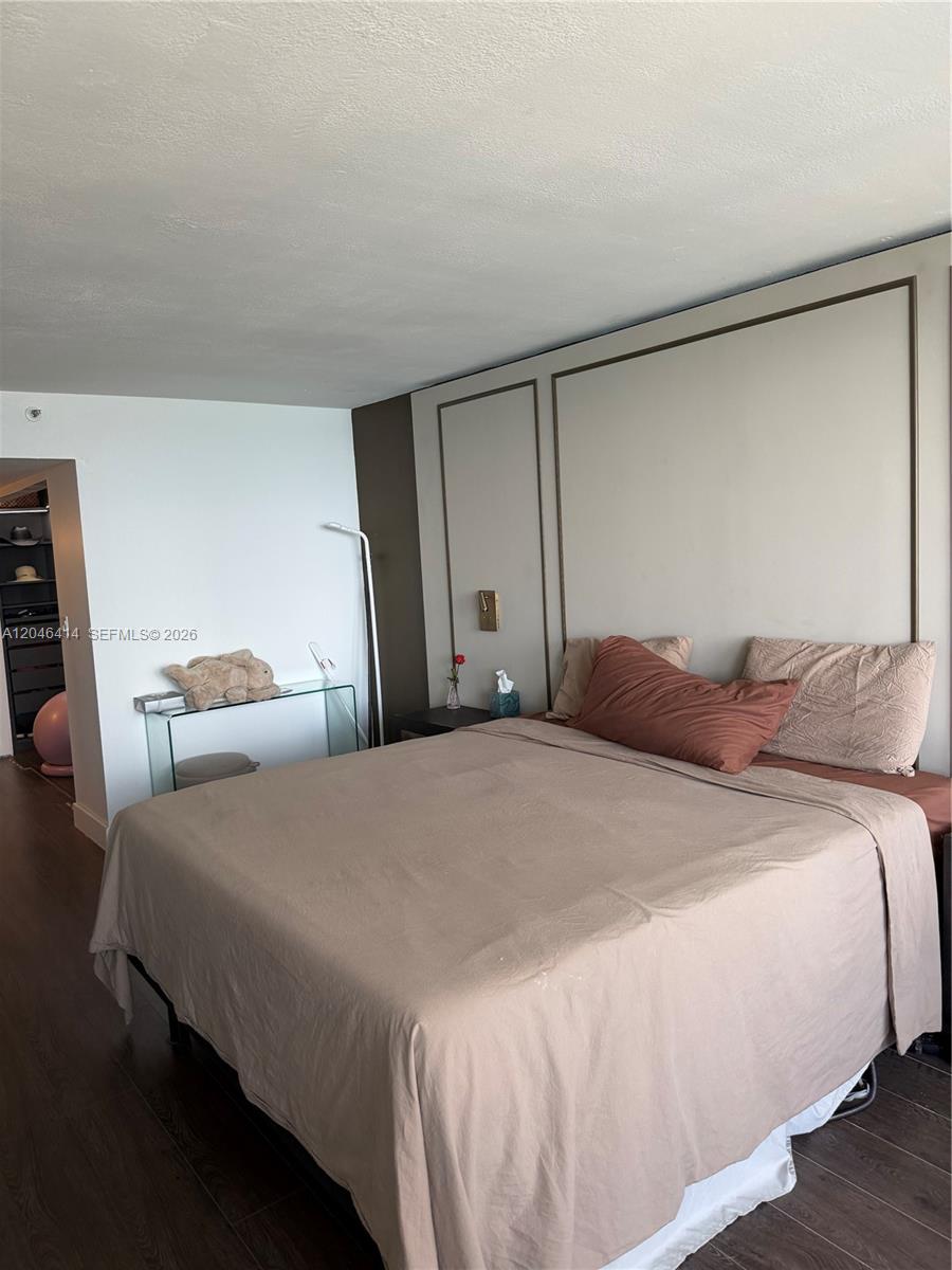 A bedroom features a bed with tan bedding, a glass console table, and dark wood flooring — 1717 N Bayshore Dr # 2847, Miami FL 33132, MIAMI, FL