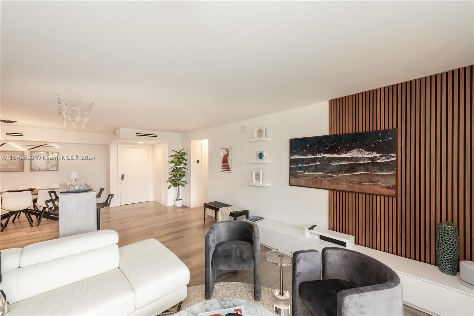 A living room features light wood flooring, a white sofa, two grey chairs, and wood-slatted wall paneling — 1111 Crandon Blvd # A306, Key Biscayne FL 33149, KEY BISCAYNE, FL