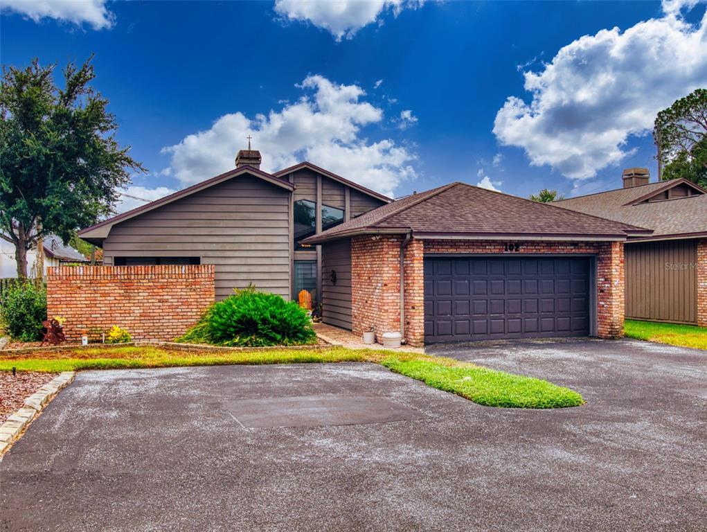 A brown house with a brick facade and a two-car garage under a cloudy sky — 102 COUNTRY PLACE, SANFORD, FL