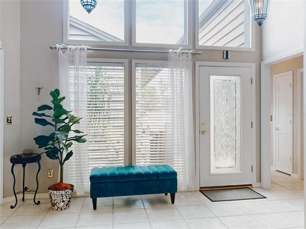 A bright entryway features a teal bench, a potted plant, and a front door with glass — 102 COUNTRY PLACE, SANFORD, FL