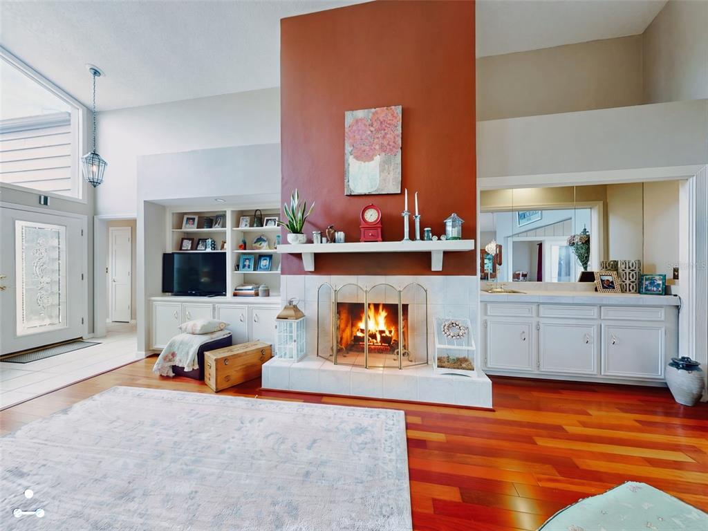 A living room features a central terracotta-colored fireplace, built-in shelving, and hardwood flooring — 102 COUNTRY PLACE, SANFORD, FL