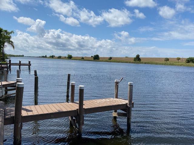A wooden dock extends into a calm canal under a blue sky with scattered clouds — 8680 Us Highway 441, Okeechobee FL 34974, OKEECHOBEE, FL