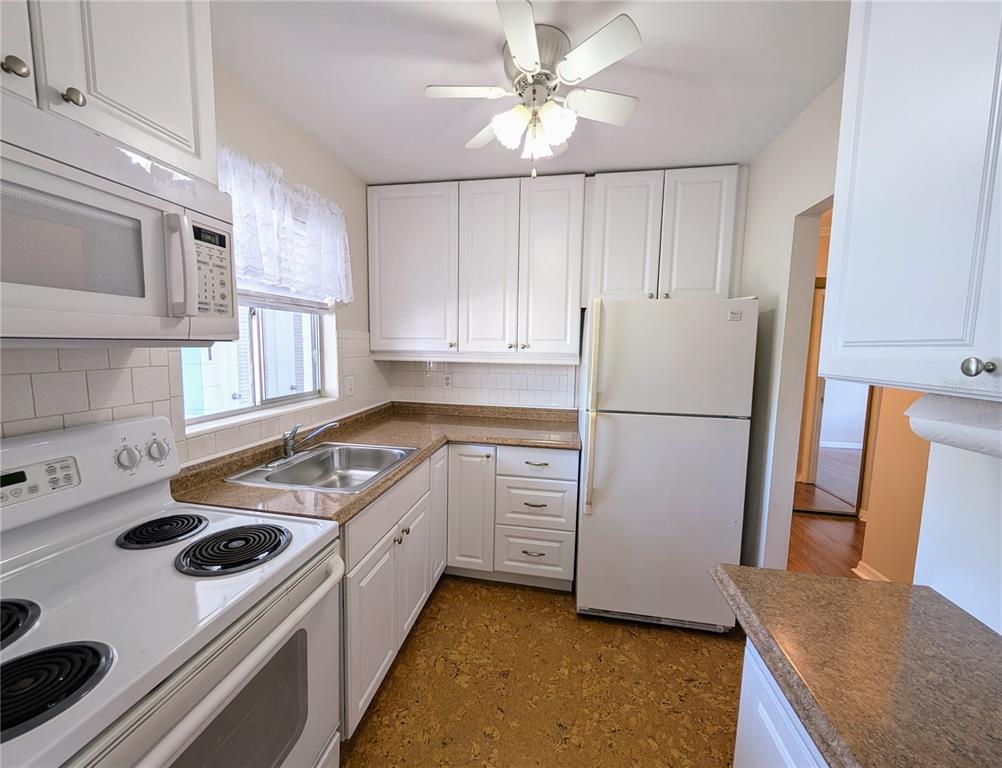 A kitchen features white cabinets, a white stove, a refrigerator, and speckled brown countertops — 1840 SUNNY DRIVE UNIT D-36, BRADENTON, FL