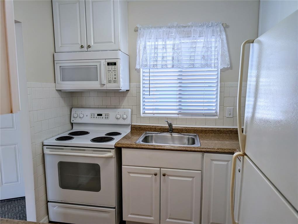 A small kitchen features white cabinets, a white stove, a microwave, and a stainless sink — 1840 SUNNY DRIVE UNIT D-36, BRADENTON, FL