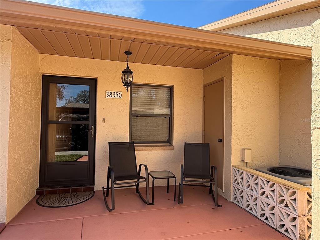 A covered patio features two rocking chairs, a small table, and a decorative concrete screen — 38350 IRONWOOD PLACE UNIT 5, ZEPHYRHILLS, FL