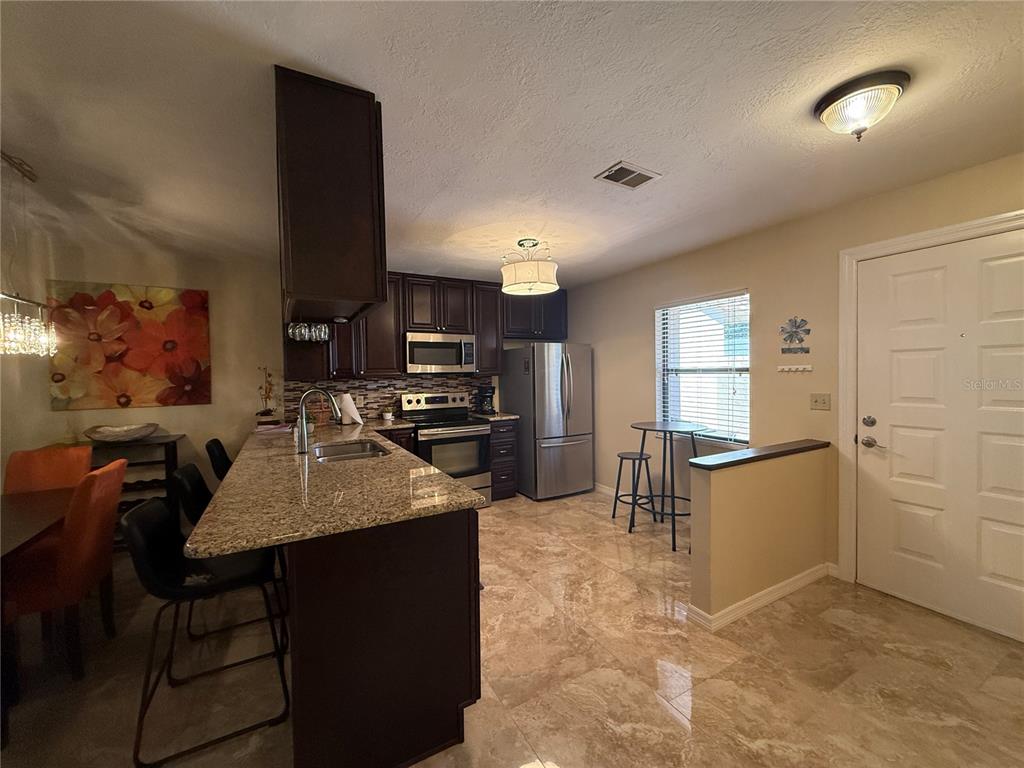 A kitchen features dark wood cabinets, granite countertops, stainless steel appliances, and tile flooring — 38350 IRONWOOD PLACE UNIT 5, ZEPHYRHILLS, FL