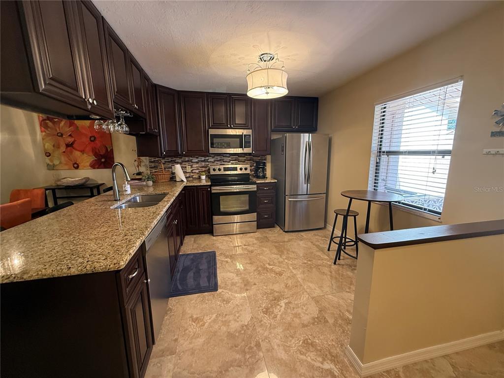 A kitchen features dark wood cabinets, granite countertops, stainless steel appliances, and tile flooring — 38350 IRONWOOD PLACE UNIT 5, ZEPHYRHILLS, FL