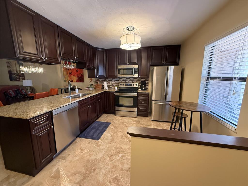 A kitchen features dark wood cabinets, granite countertops, stainless steel appliances, and tile flooring — 38350 IRONWOOD PLACE UNIT 5, ZEPHYRHILLS, FL