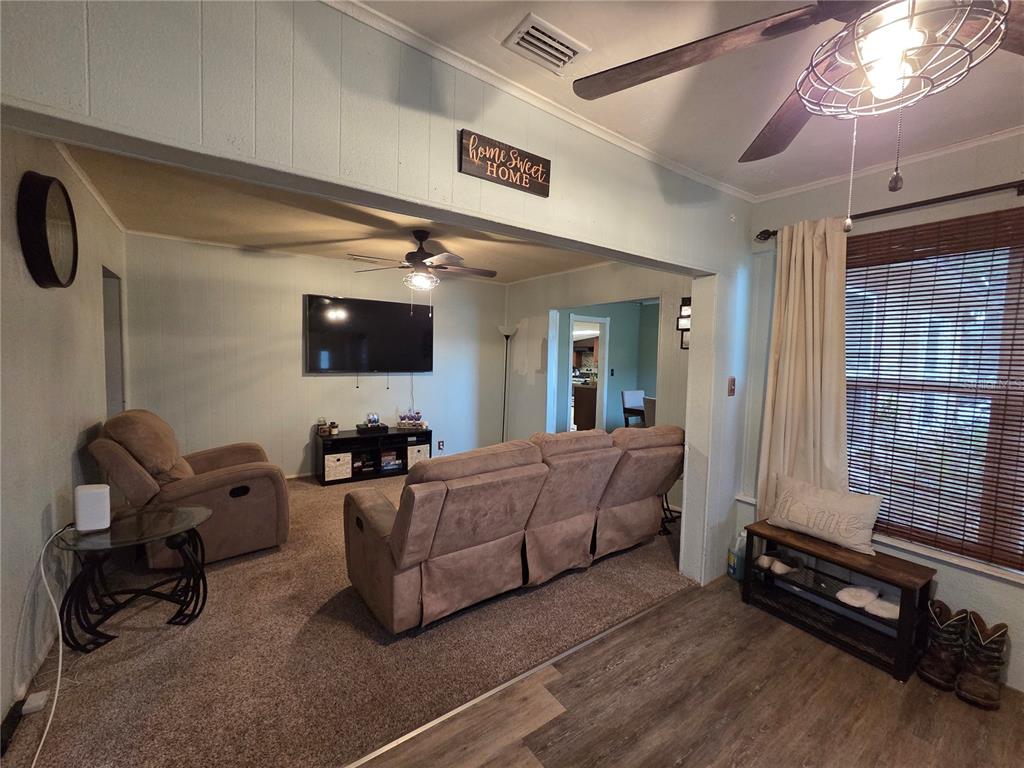 A living room features carpeted flooring, a wall-mounted television, and a beige reclining sofa — 124 E F ST, FROSTPROOF, FL