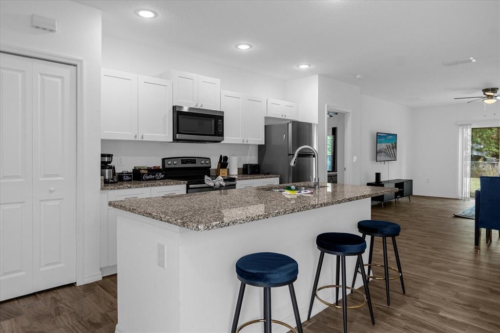 A kitchen with white cabinets, granite countertops, and an island with blue bar stools — 97 N GOLDWYN AVENUE, ORLANDO, FL