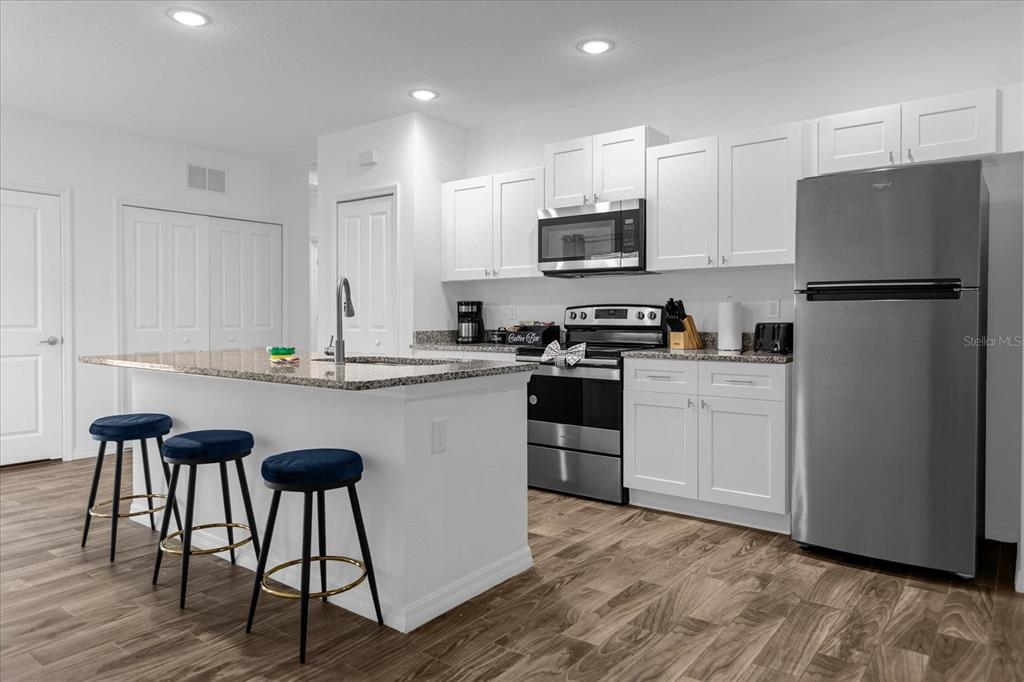 A modern kitchen features white cabinetry, granite countertops, stainless steel appliances, and a breakfast island — 97 N GOLDWYN AVENUE, ORLANDO, FL