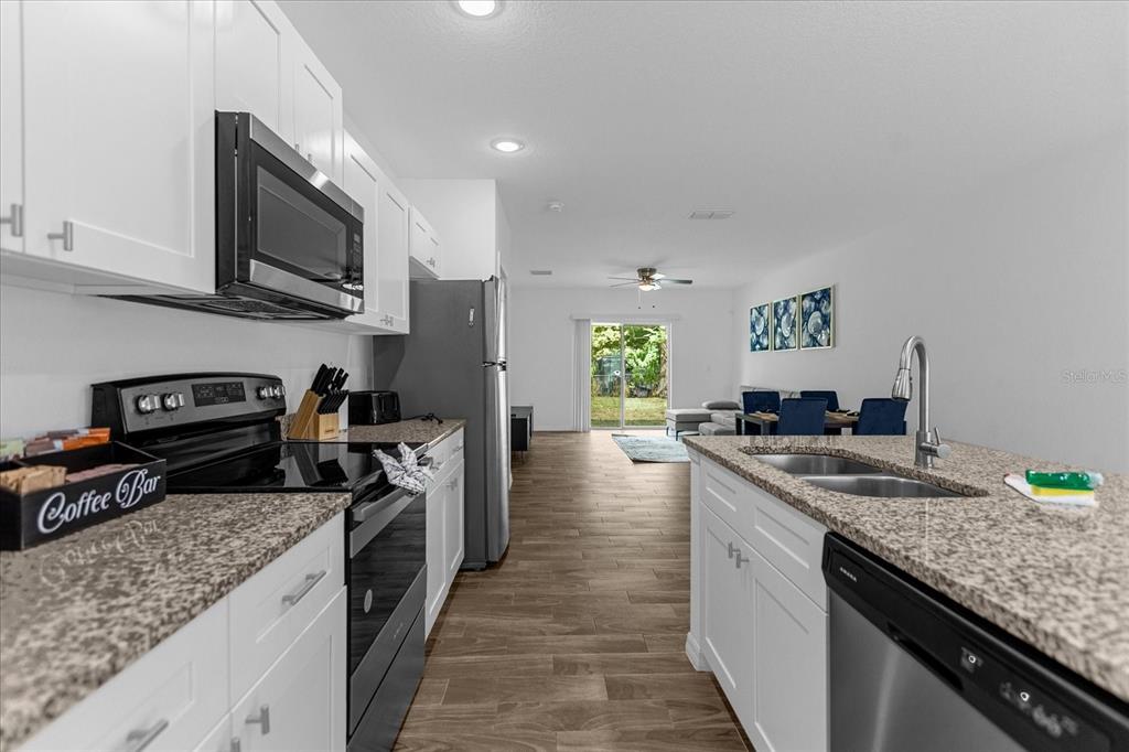 A kitchen with white cabinets, granite countertops, and stainless steel appliances overlooks an open living area — 97 N GOLDWYN AVENUE, ORLANDO, FL
