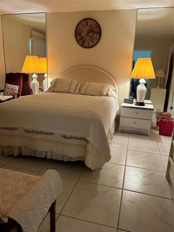 A bedroom features a bed with a quilted cover, two nightstands, and large wall mirrors — 4090 NW 42ND AVENUE UNIT 105, FORT LAUDERDALE, FL