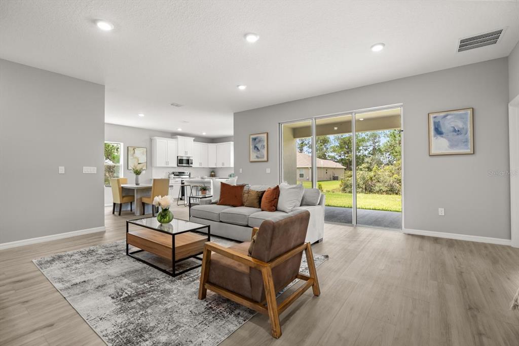 A living room with light wood floors, a grey sofa, and an open kitchen area — 5336 COLUMBUS BOULEVARD, SEBRING, FL