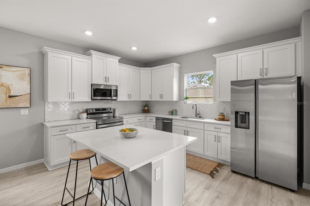 A modern kitchen features white cabinetry, stainless steel appliances, a center island, and light flooring — 5336 COLUMBUS BOULEVARD, SEBRING, FL