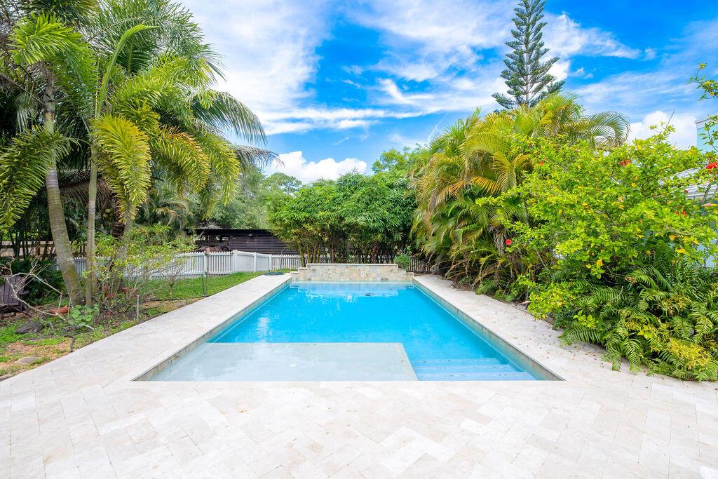 A rectangular swimming pool with a stone patio is surrounded by lush tropical landscaping — 16215 121st Terrace N, Jupiter FL 33478, JUPITER, FL