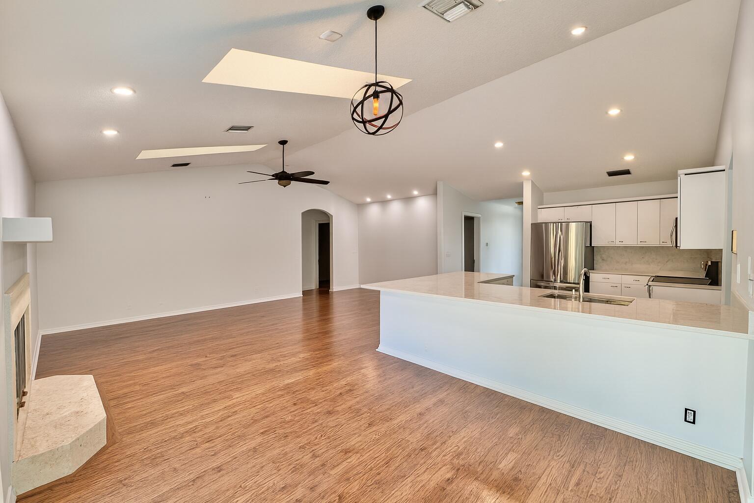 A bright, open-concept living room and kitchen featuring vaulted ceilings, skylights, and wood flooring — 16215 121st Terrace N, Jupiter FL 33478, JUPITER, FL