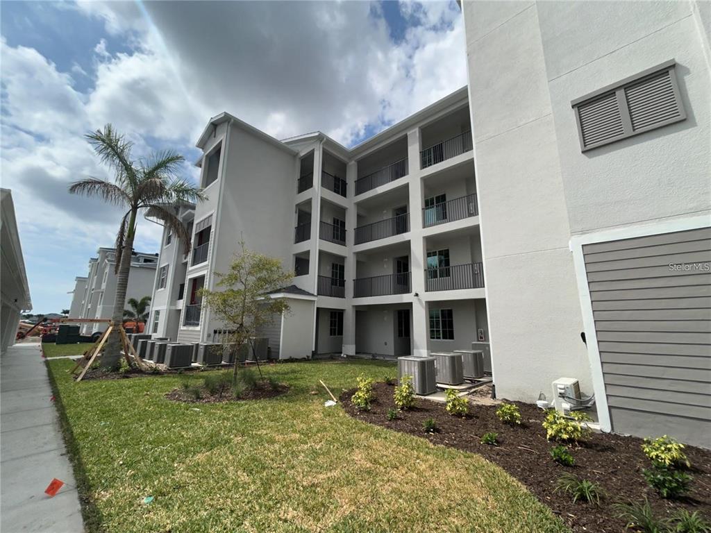 A multi-story apartment building exterior features balconies, gray siding, and ground-level air conditioning units — 12240 WELLEN GOLF STREET UNIT 403, VENICE, FL