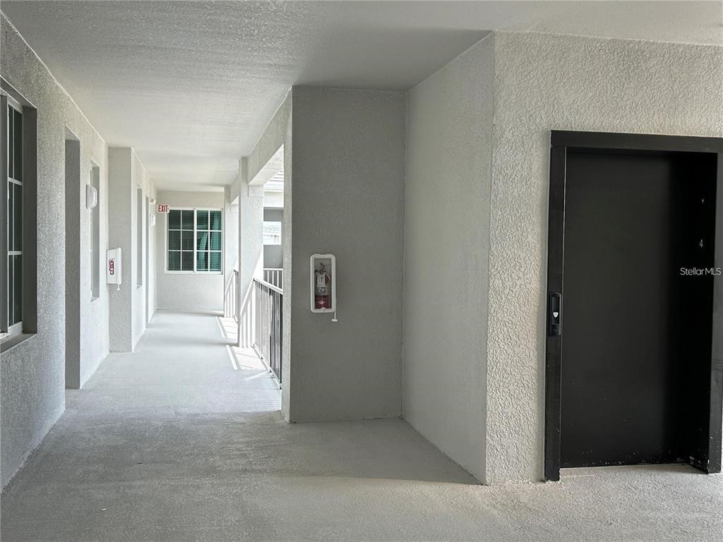 An outdoor apartment hallway features a black door, a fire extinguisher, and a window — 12240 WELLEN GOLF STREET UNIT 403, VENICE, FL