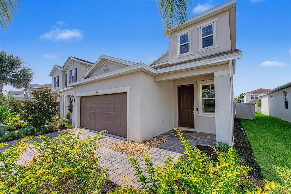 A two-story suburban house features a tan stucco exterior, a two-car garage, and a paved walkway — 5435 BUNGALOW GROVE COURT, PALMETTO, FL