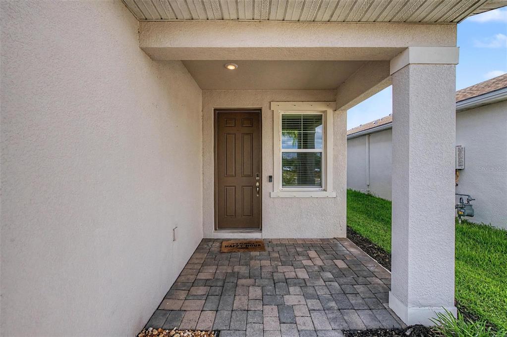 A covered entryway features a brown front door, a window, and a paved stone floor — 5435 BUNGALOW GROVE COURT, PALMETTO, FL