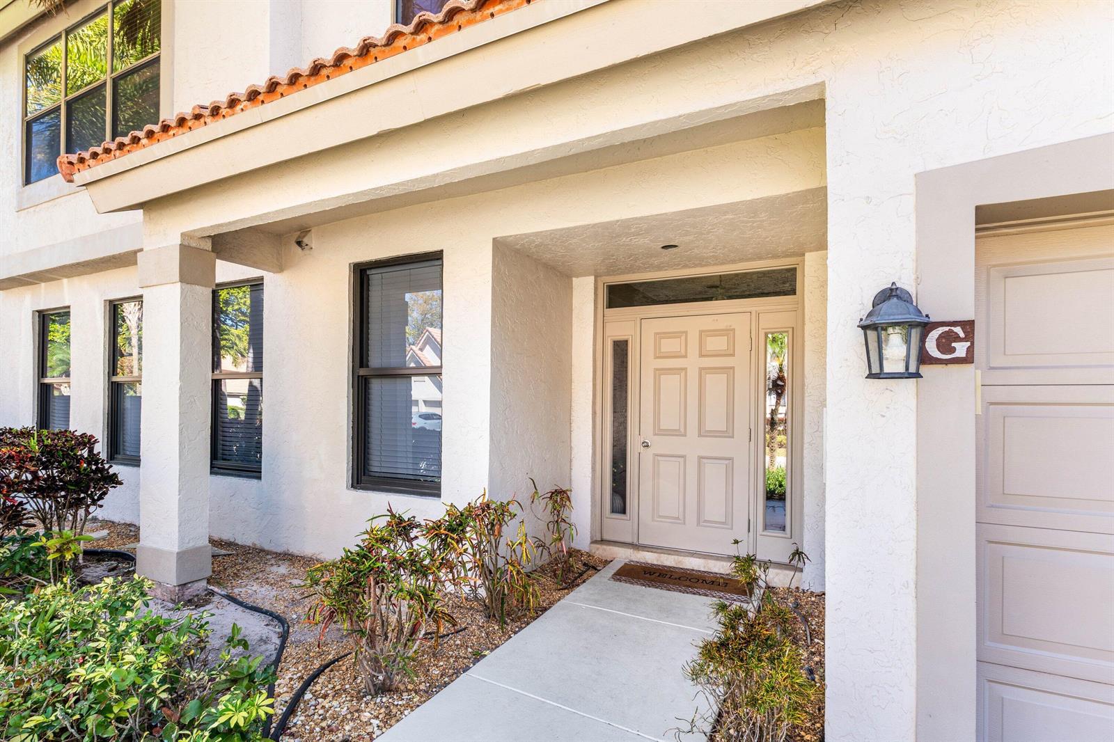 The exterior of a white stucco home features a front door, walkway, and landscaping — 5780 Coach House Circle # C, Boca Raton FL 33486, BOCA RATON, FL
