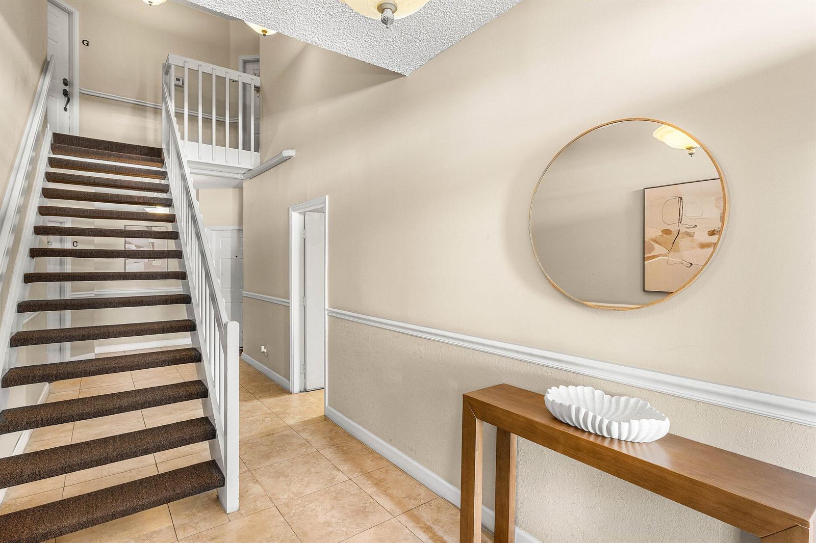 An entryway features a staircase with brown carpet, tile flooring, a console table, and mirror — 5780 Coach House Circle # C, Boca Raton FL 33486, BOCA RATON, FL