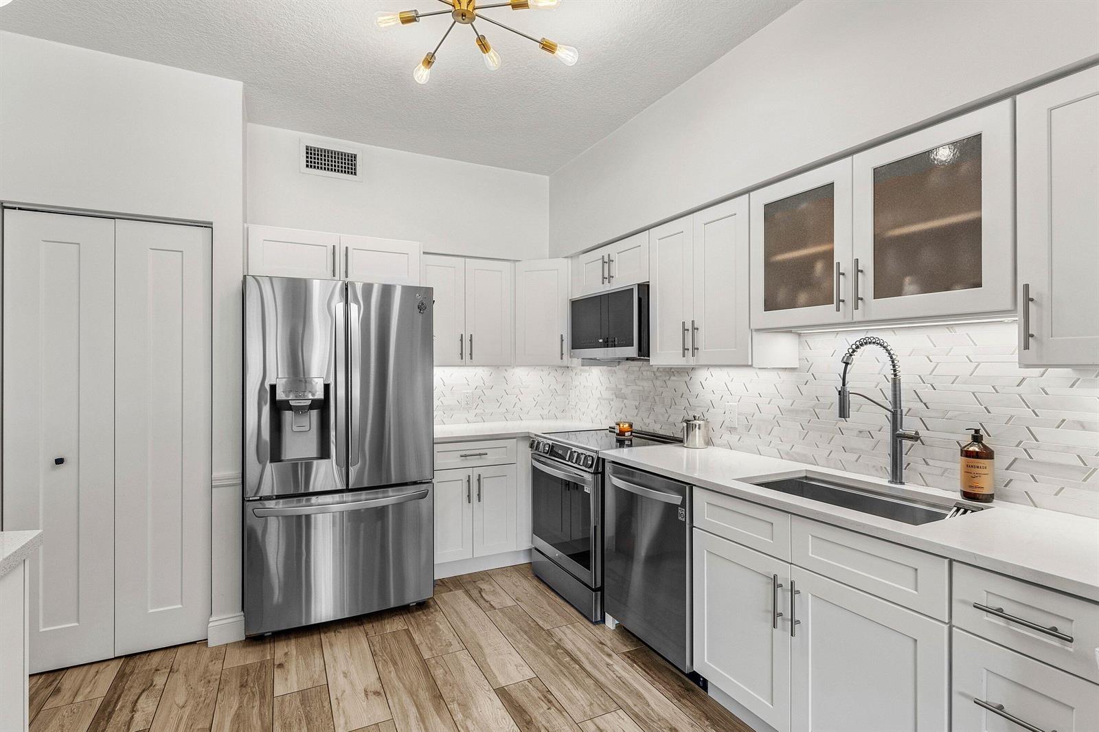A modern kitchen features white cabinets, stainless steel appliances, a tiled backsplash, and wood flooring — 5780 Coach House Circle # C, Boca Raton FL 33486, BOCA RATON, FL