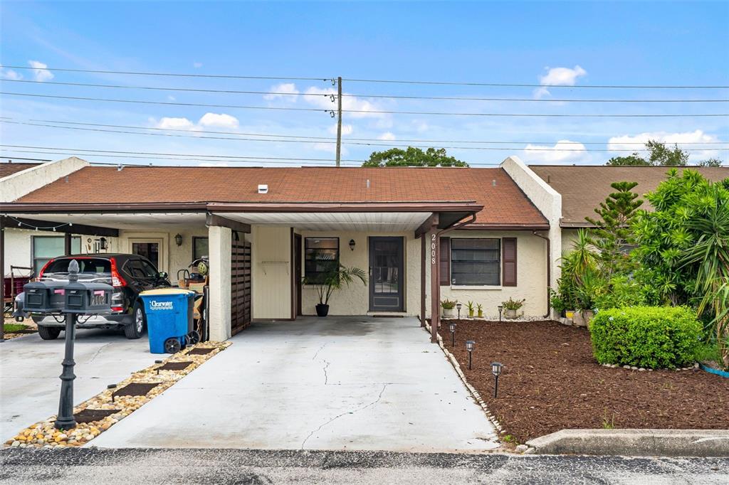 A single-story house exterior features a concrete driveway, a covered carport, and a front garden — 2008 SUNSET GROVE LANE, CLEARWATER, FL