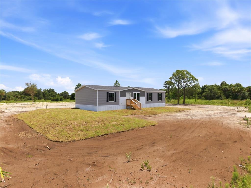 A single-story manufactured home sits on a cleared, sandy lot under a blue sky — 17975 NW 266TH STREET, OKEECHOBEE, FL