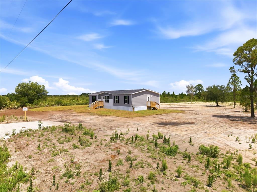 A single-story manufactured home sits on a large, cleared dirt lot under a blue sky — 17975 NW 266TH STREET, OKEECHOBEE, FL