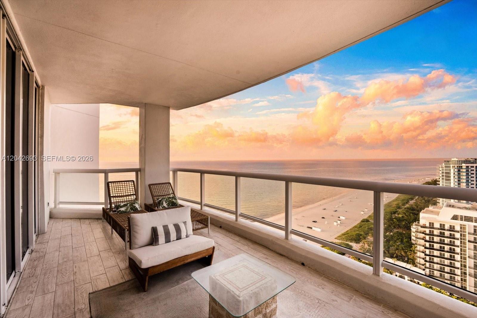 A balcony with outdoor seating overlooks the ocean and beach at sunset — 4201 Collins Ave # 2301, Miami Beach FL 33140, MIAMI BEACH, FL