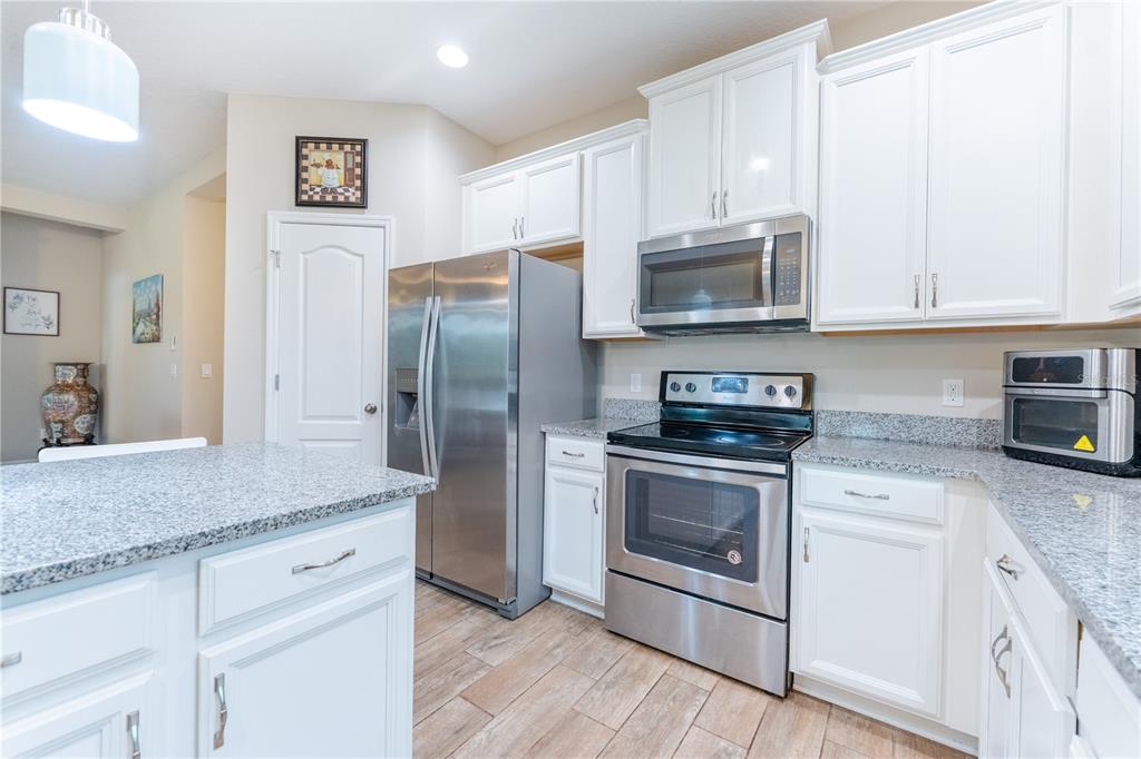 A kitchen features white cabinets, stainless steel appliances, granite countertops, and wood-look tile flooring — 3331 SAGEBRUSH STREET, HARMONY, FL
