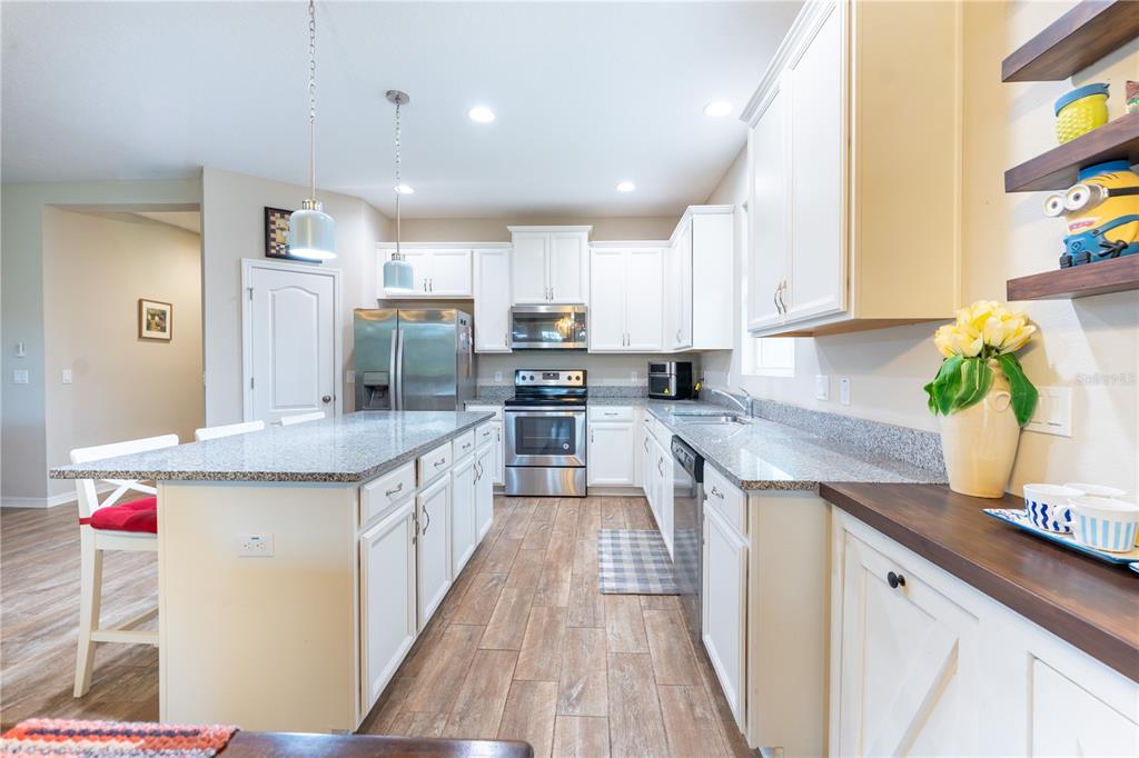 A kitchen features white cabinetry, granite countertops, stainless steel appliances, and a central island — 3331 SAGEBRUSH STREET, HARMONY, FL