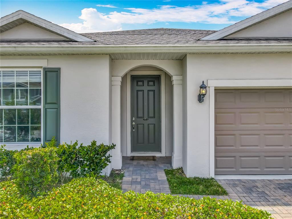 The exterior of a house features a dark green front door, a garage, and landscaping — 2610 HILLTOP LOOP, APOPKA, FL