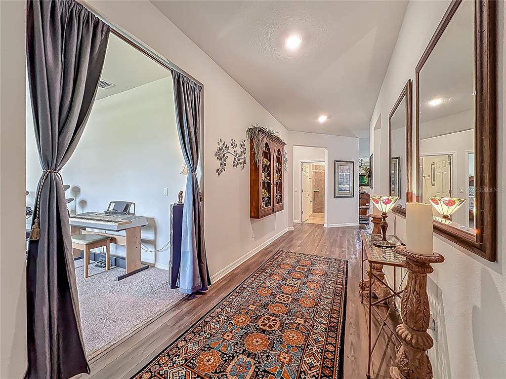 A hallway with wood-look flooring, a patterned runner rug, and a mirrored wall console table — 2610 HILLTOP LOOP, APOPKA, FL