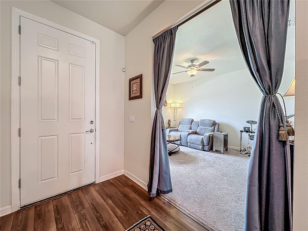 An entryway with wood-look flooring leads into a carpeted living room through a curtained opening — 2610 HILLTOP LOOP, APOPKA, FL