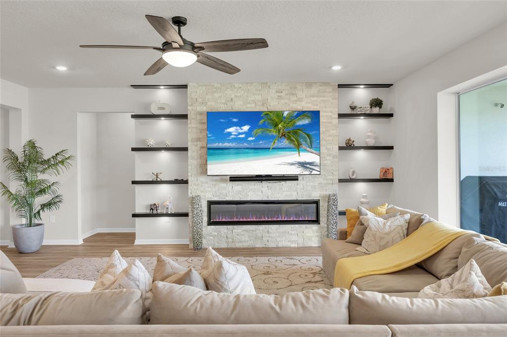 A living room features a stone fireplace wall with a mounted television and built-in shelves — 3286 MAINSAIL COURT, WINTER GARDEN, FL