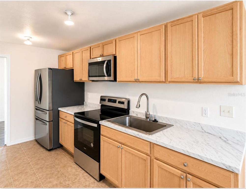 A kitchen features light wood cabinets, stainless steel appliances, and white marble-patterned countertops — 301 CLARK STREET UNIT 2, MAITLAND, FL