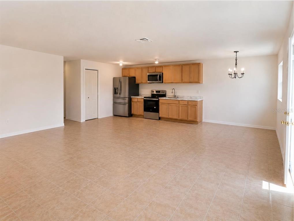 An open-concept kitchen features light wood cabinets, stainless steel appliances, and beige tile flooring — 301 CLARK STREET UNIT 2, MAITLAND, FL
