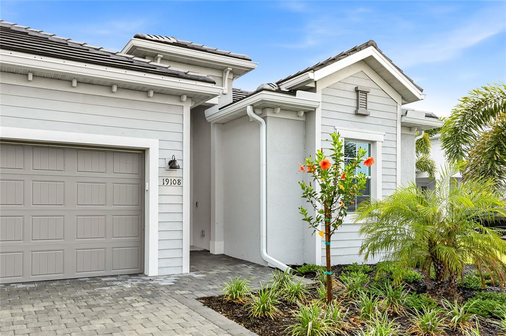The exterior of a light gray house features a garage, a paved driveway, and landscaping — 19108 CHERRYSTONE WAY, LAKEWOOD RANCH, FL