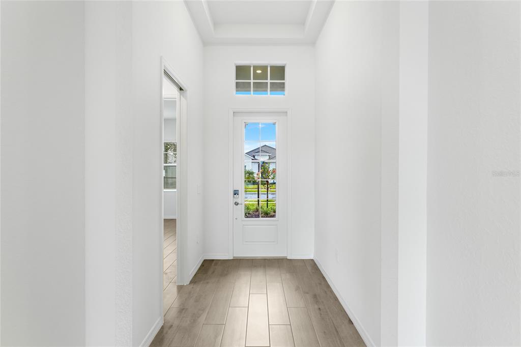 A bright entryway features white walls, wood-look tile flooring, and a glass-paneled front door — 19108 CHERRYSTONE WAY, LAKEWOOD RANCH, FL