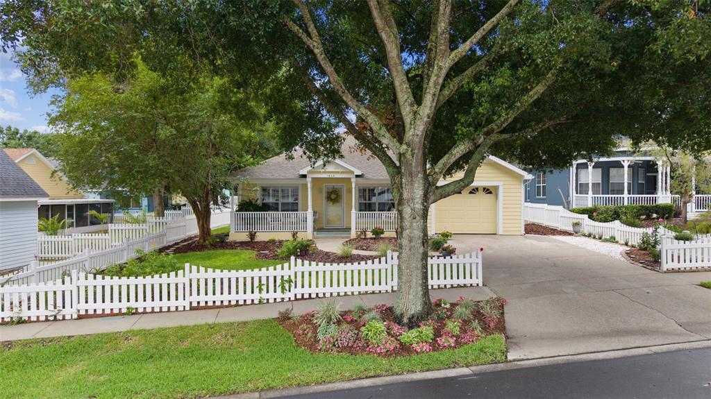 A yellow house with a white picket fence and a large tree in the front yard — 1622 LAUREL WAY, TAVARES, FL