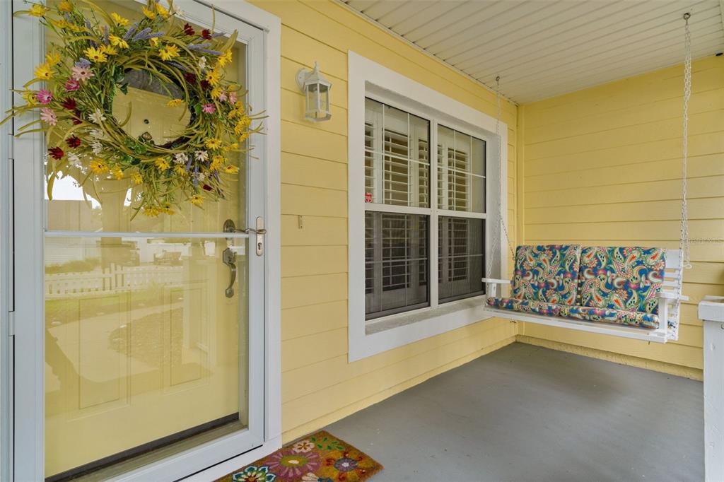 A yellow-sided front porch features a floral wreath on the door and a hanging swing — 1622 LAUREL WAY, TAVARES, FL